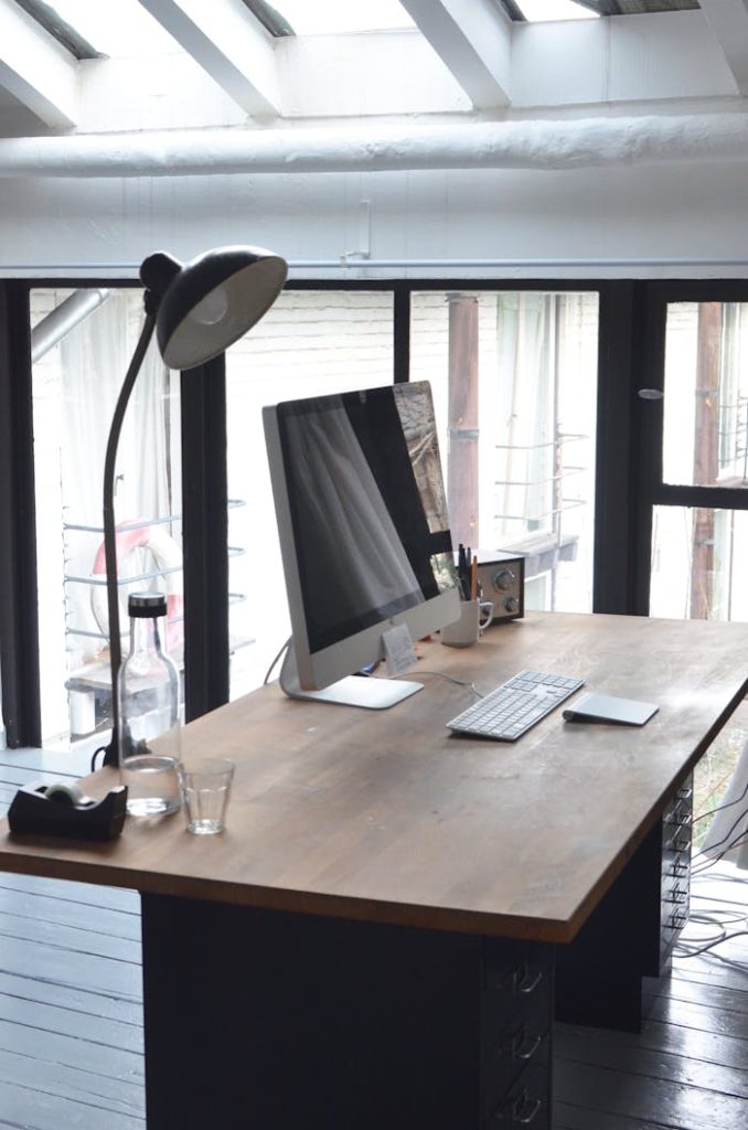 A sleek, minimalist office setup featuring a computer on a wooden desk with natural daylight.